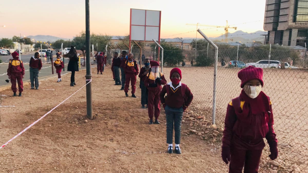lapset jonottavat turvavälein koulun pihalla Windhoekissa, Namibiassa