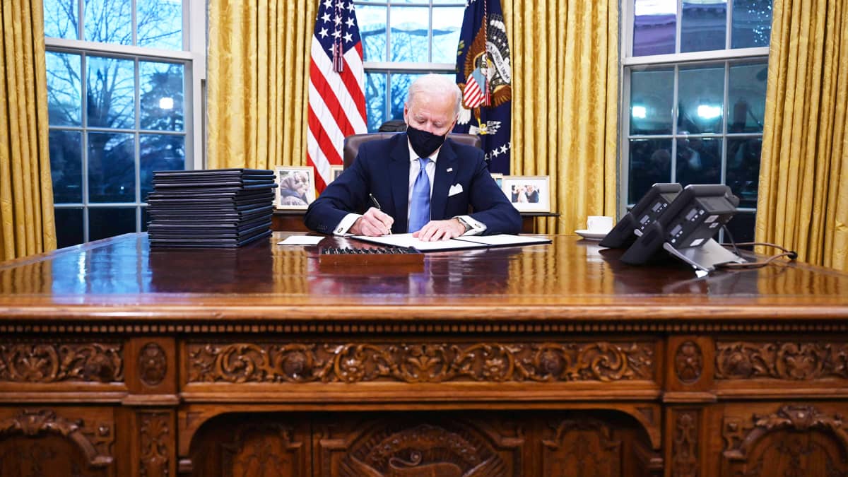 Joe Biden allekirjoittaa papereita Valkoisessa talossa.