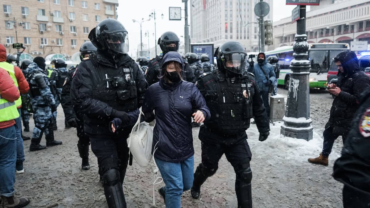 Poliisi kiinni ottamaa henkilö viedää poliisiautoon.