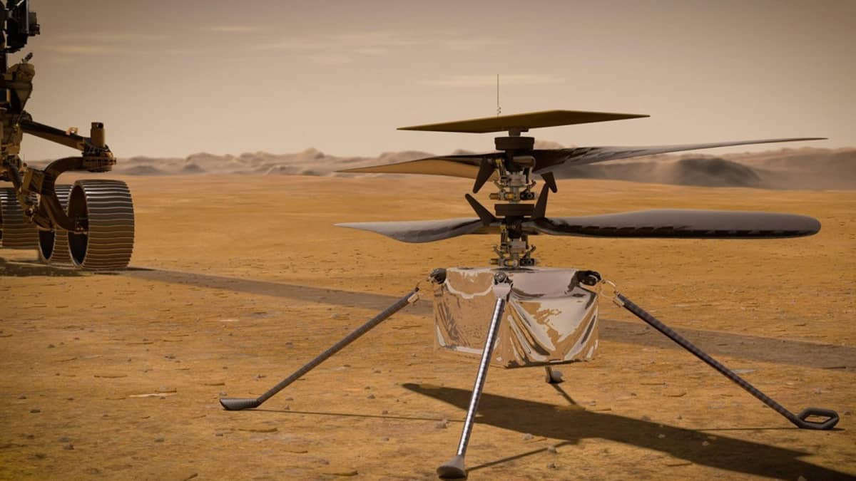 Neljällä pitkällä jalalla seisova laatikon muotoinen helikopteri Marsin punaisella pinnalla. Taustalla kuvasta rullaa pois mönkijä. 