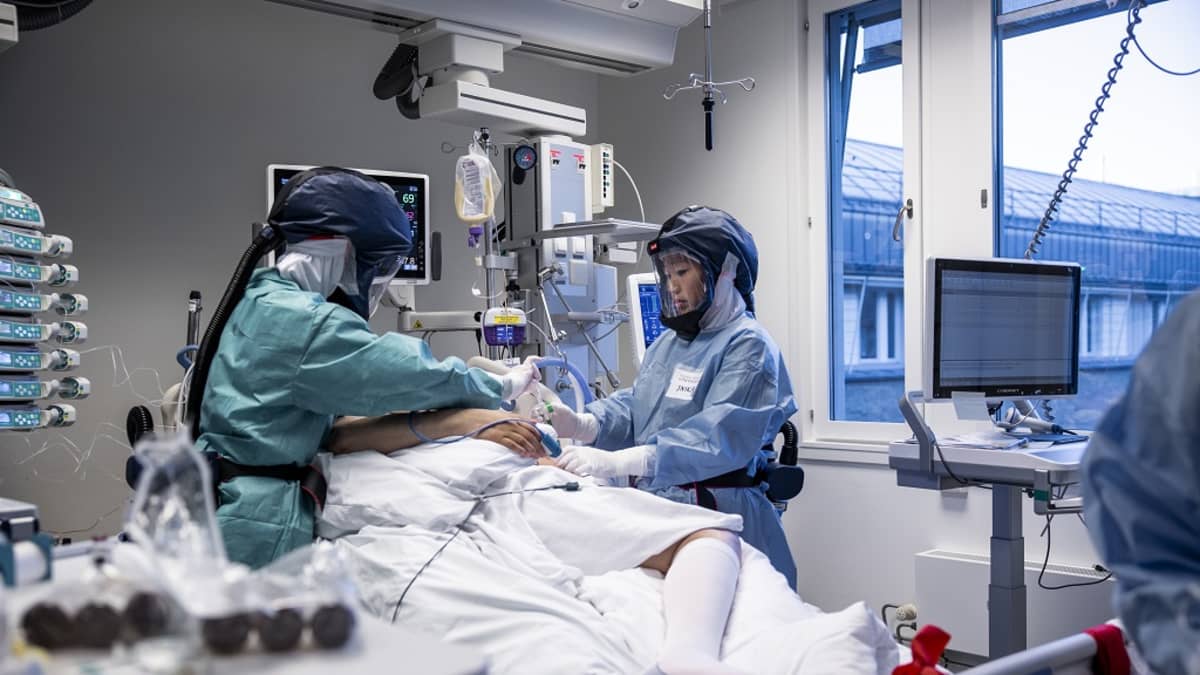 Suojavarusteiset työntekijät potilasvuoteen molemmin puolin.