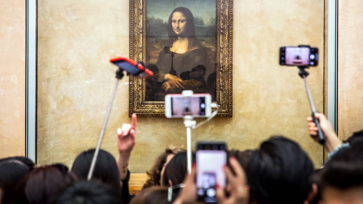Museovieraat valokuvaavat naista esittävää öljyvärimaalausta Louvressa.
