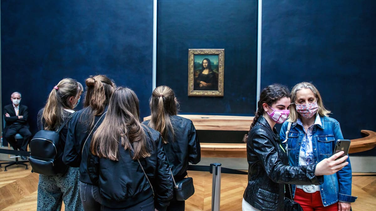 Museovieraa valokuvaavat itseään naista esittävän öljymaalauksen edessä Louvressa.