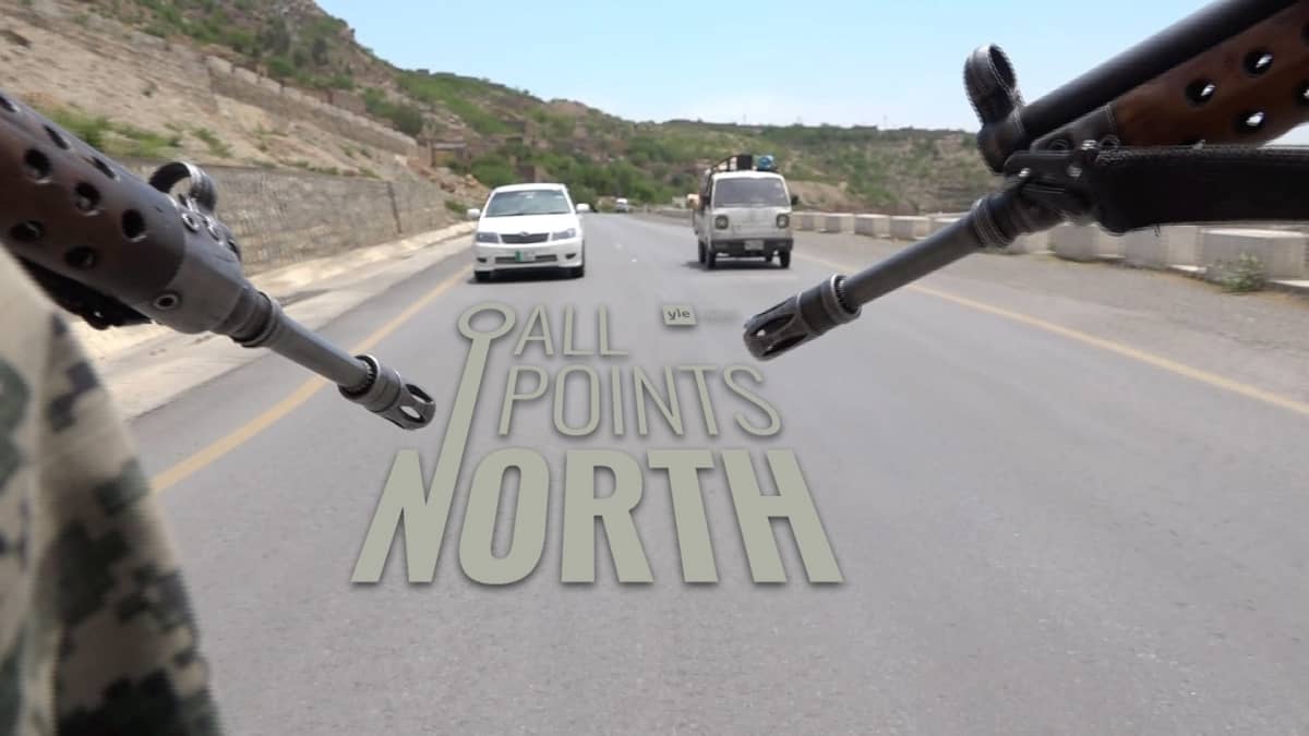 Video still of two rifles pointed from the back of a vehicle driving along a road in Afghanistan featuring the All Points North Podcast logo.