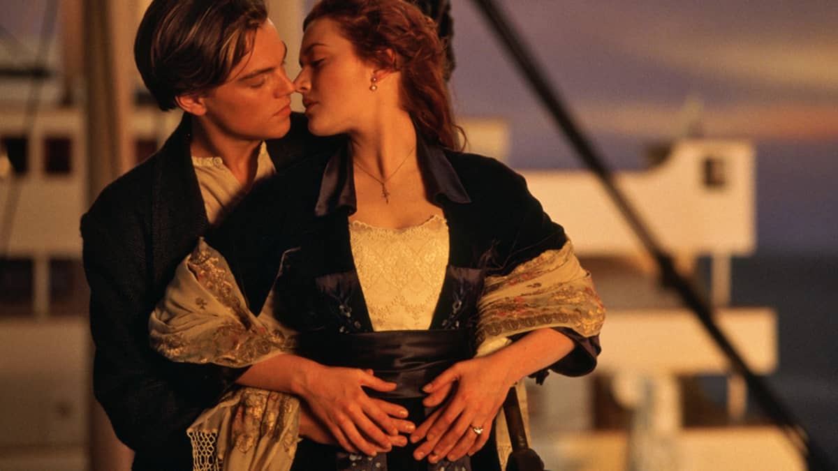 Näyttelijät Leonardo DiCaprio ja Kate Winslet suutelevat Titanicin kannella auringon laskiessa.