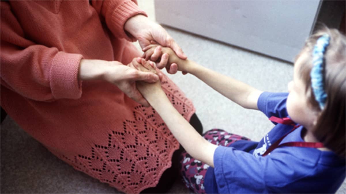 Äiti ja lapsi istuvat lattialla pitäen toisiaan käsistä