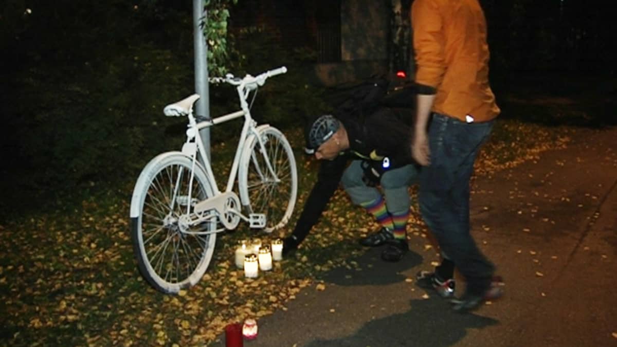 Miehet asettavat hautakynttilöitä valkoiseksi maalatun pyörän juurelle.