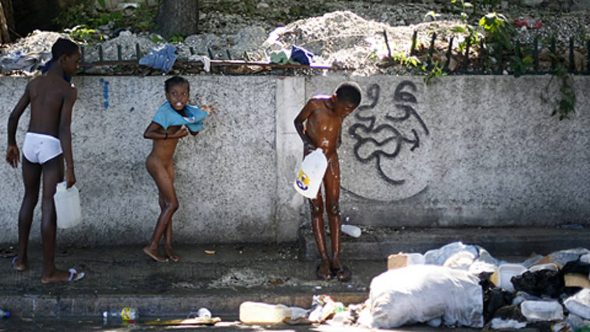 Kodittomia lapsia peseytyy säiliöstä kaatamansa veden alla kadulla Port-au-Princessä.