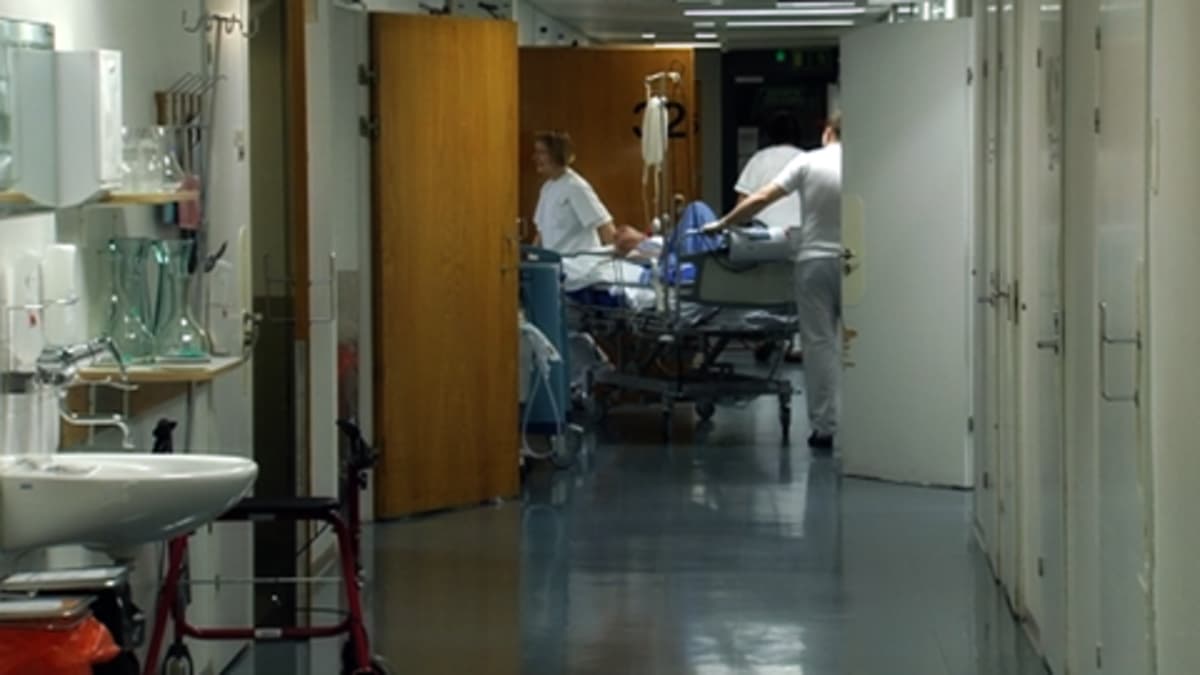Kolme sairaanhoitajaa työntää sänkyä sairaalan tyhjällä käytävällä.