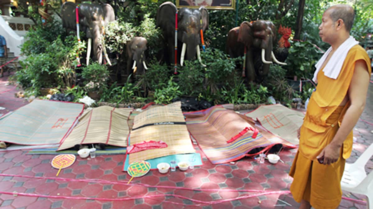 Thaimaalainen buddhalaismunkki katsoo peiteltyjä  ruumiita Pathumwanaramin temppelissä torstaina.