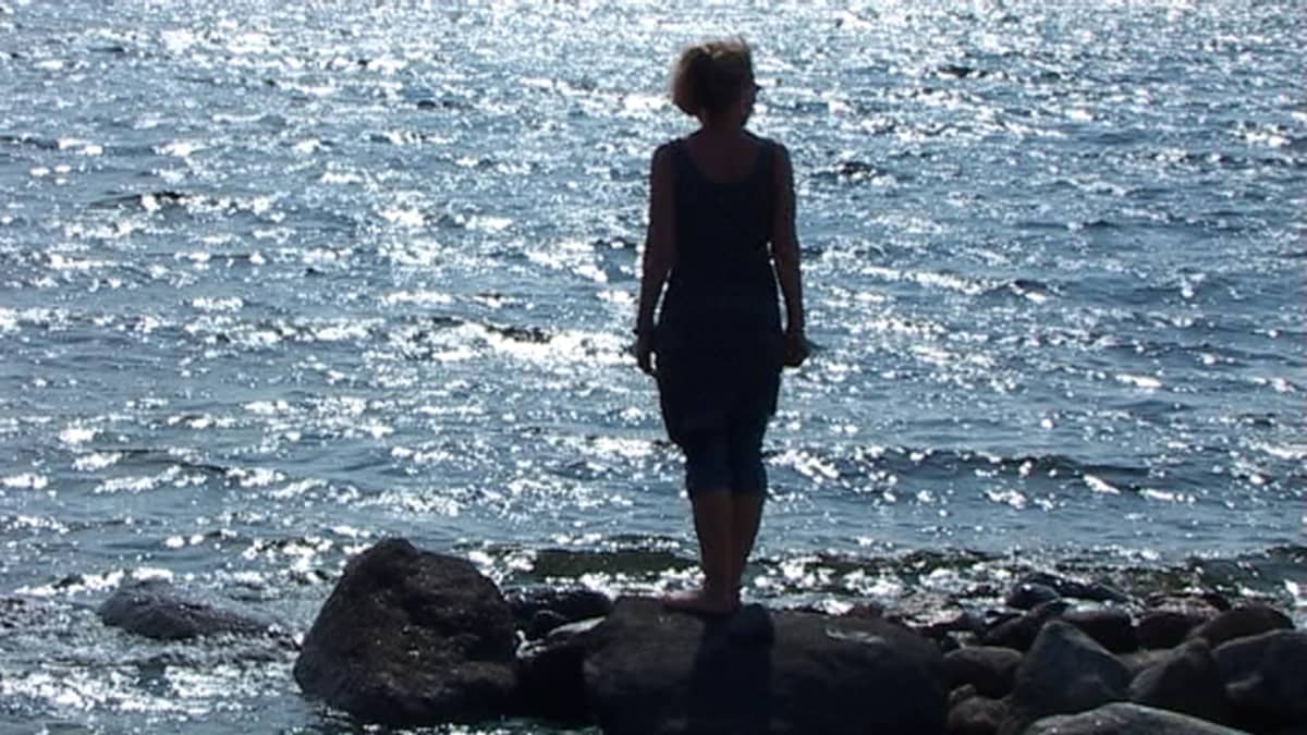 Naisen silhuetti merta vasten.
