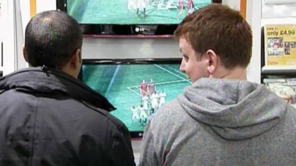 Kaksi nuorta miestä kokeilee FIFA 11 -jalkapallopeliä liikkeessä.