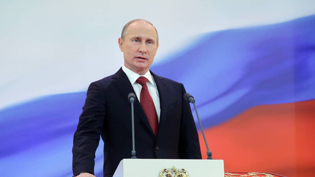 Putin vannomassa valaa puhujankorokkeella, taustalla Venäjän lipun värit.