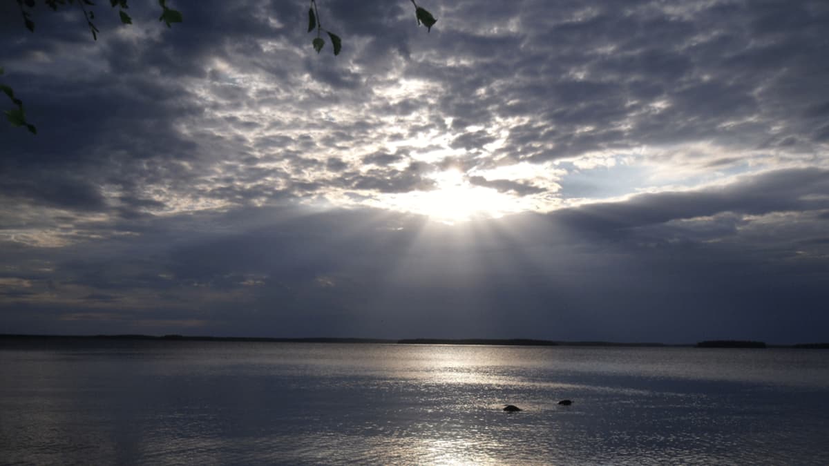 Aurinko paistaa pilvien raosta veteen