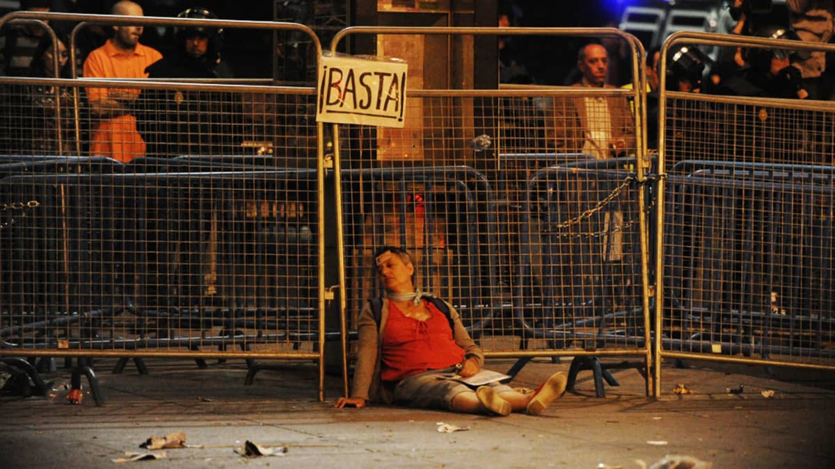 Loukkaantunut nainen nojaa mellakka-aitoihin talouskriisin vaikutuksia vastaan protestoineen mielenosoituksen aikana.