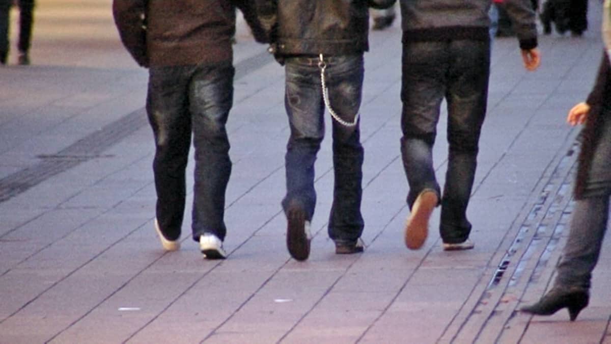 Kolme nuorta miestä kävelee kadulla. Kuva takaapäin.