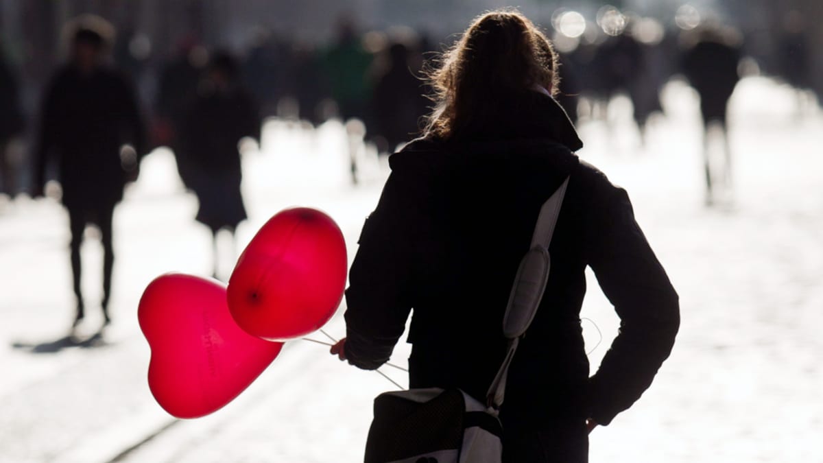 Nainen kantaa sydämen muotoisia ilmapalloja kadulla.