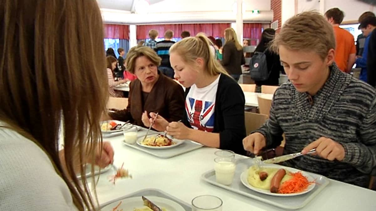 Ihmiset syövät kouluruokalassa uunimakkaraa.