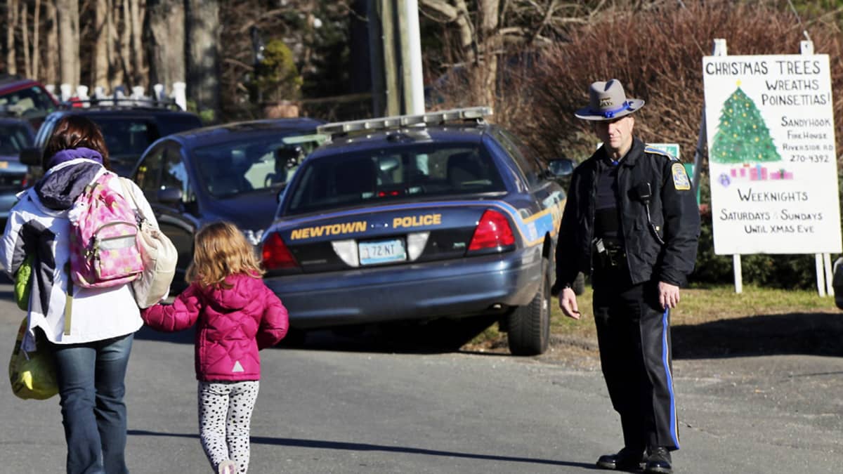 Nainen ja lapsi kävelevät poispäin, poliisi seisoo vieressä.