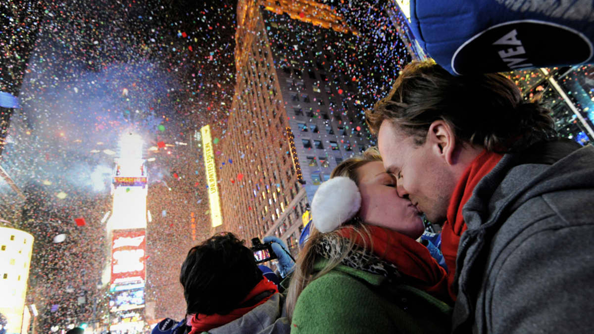 Pari suutelee kadulla, taustalla uudenvuodenjuhlintaa.