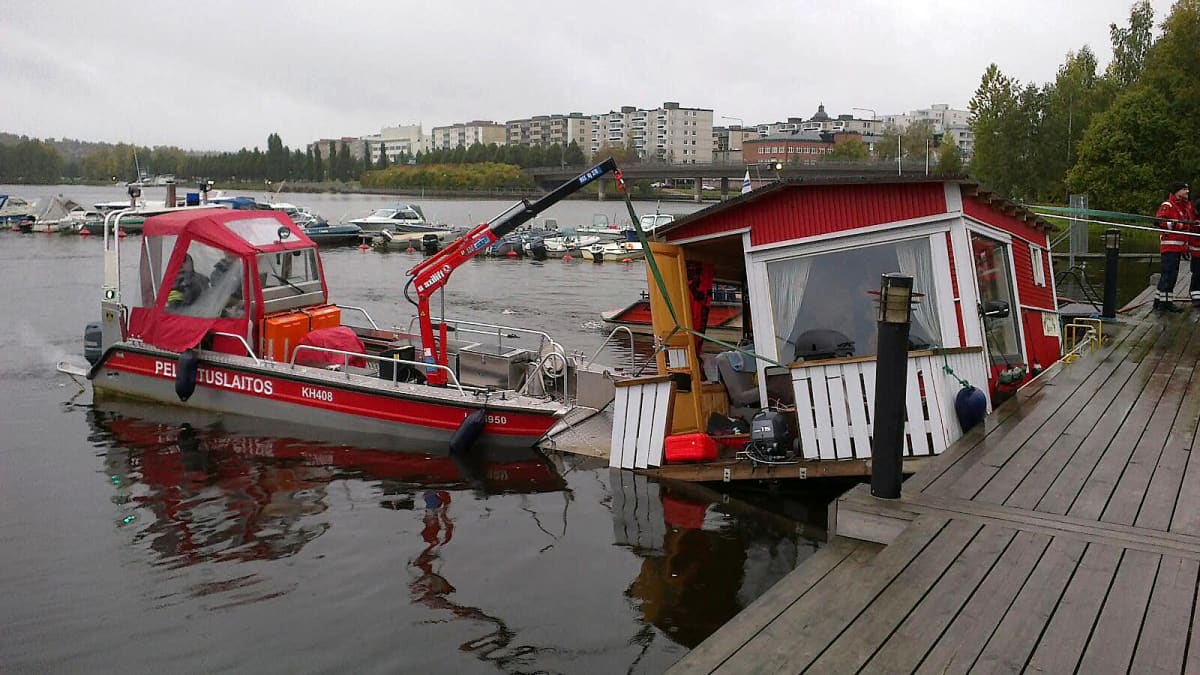 Uppoava pieni asuntolaiva, jota pelastuslaitoksen vene kannattelee