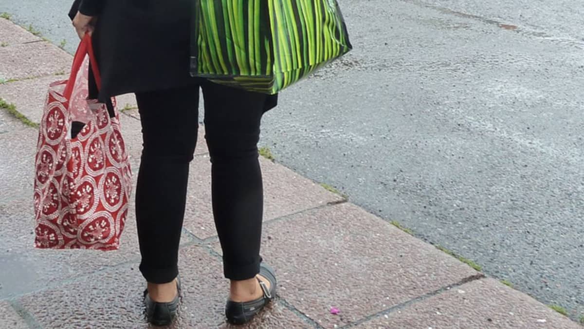 Nainen seisoo kadulla kestokassit käsissään.