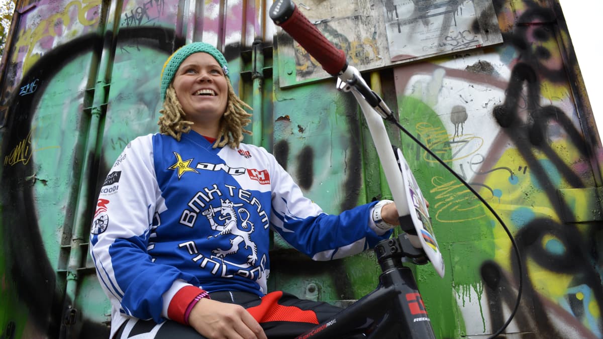 Bmx-kuljettaja Outi Leinonen istuu pyöränsä päällä ja nojaa seinään.