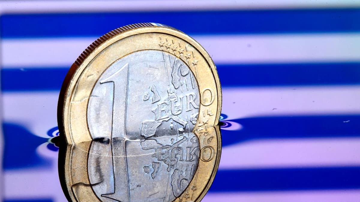 Euron kolikko vedessä, jonka pinnasta heijastuu kreikan lippu.