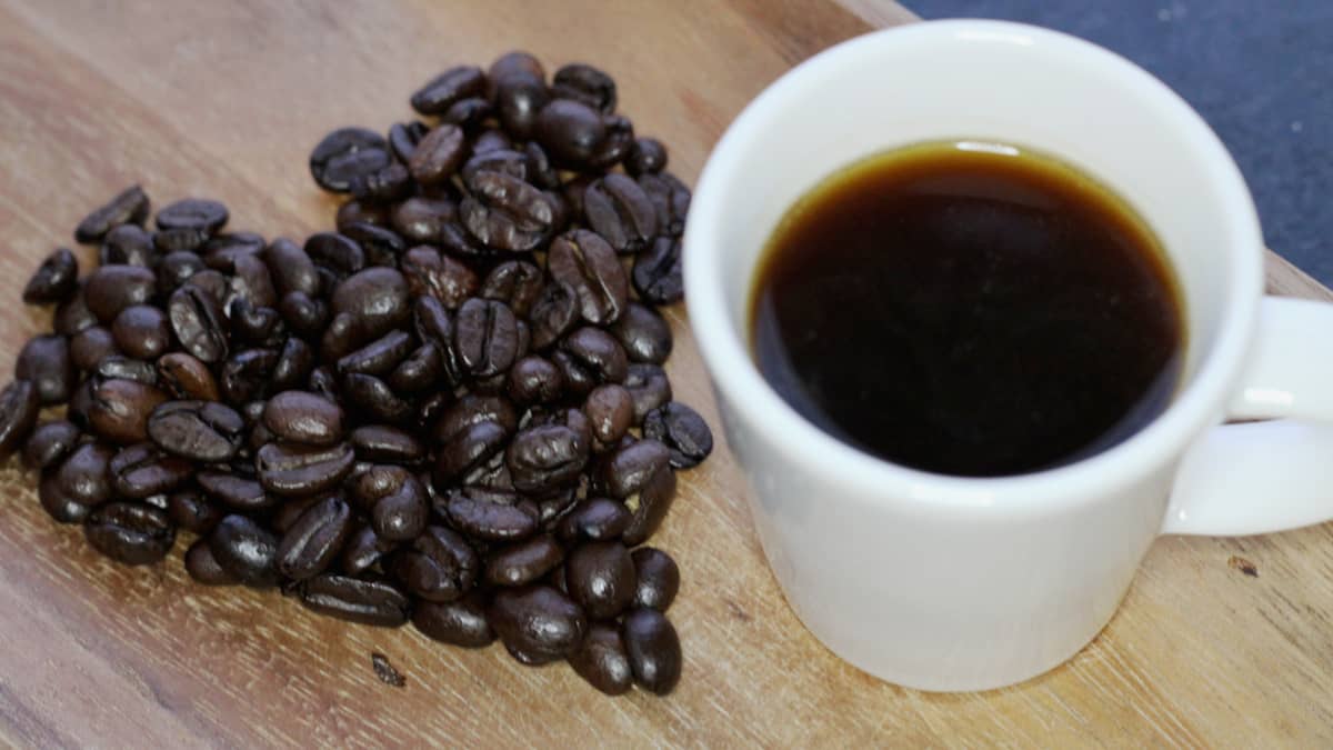 Kuvassa kupillinen kahvia ja kahvipavuista tehty sydän. 