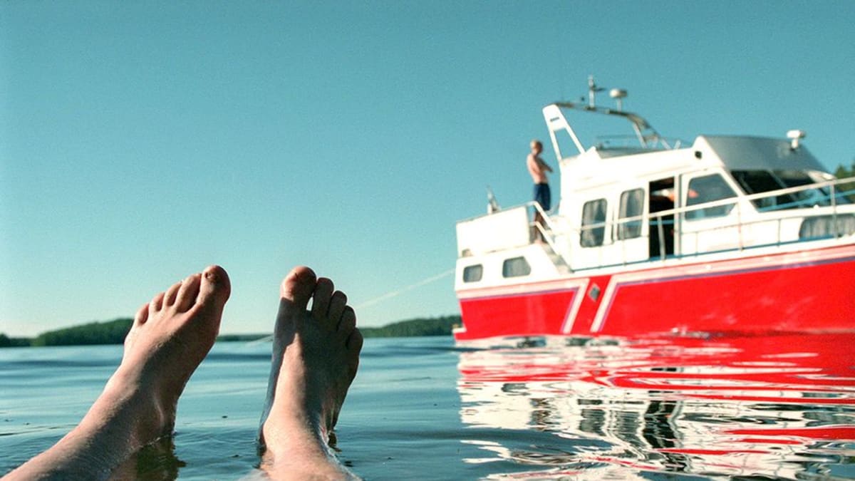 Miehen jalat veden pinnalla, taustalla punainen vene rantautuneena.