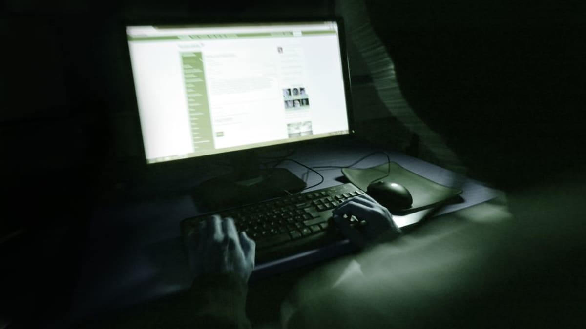 Huppupäinen hehnkilö istuu tietokoneen ääressä pimeässä.