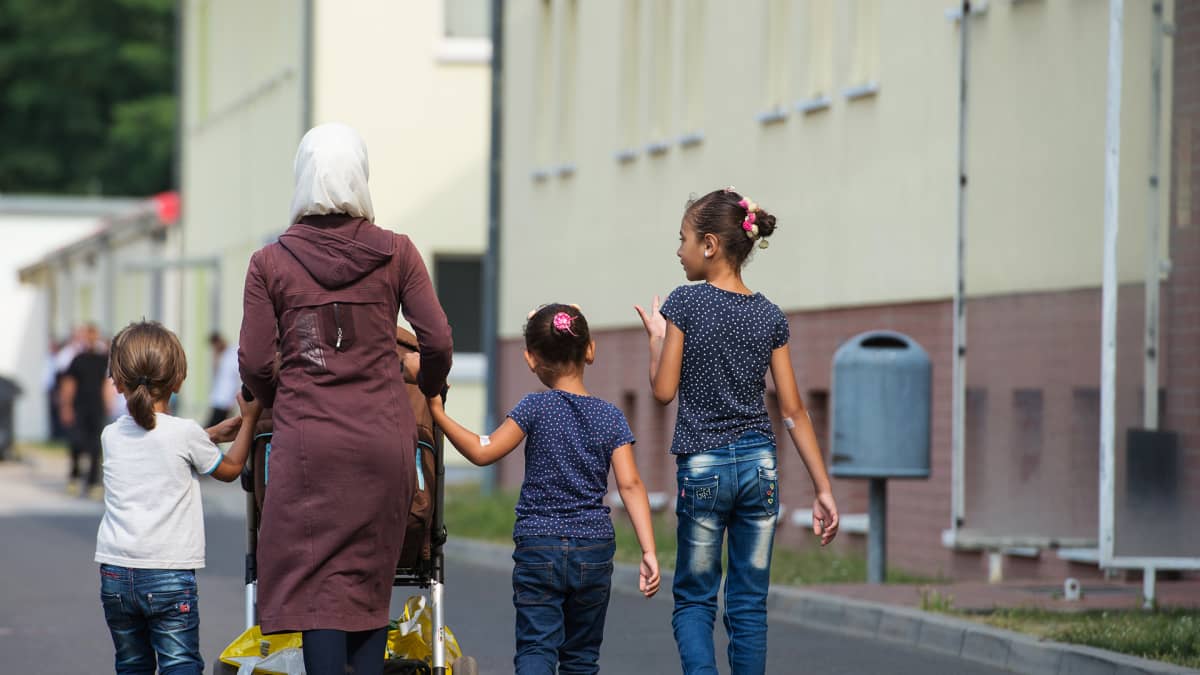 Pakolaisperhe – äiti lapsineen – kävelee turvapaikanhakijoiden käsittelykeskuksen ulkopuolella Saksan Eisenhüttenstadtissa.