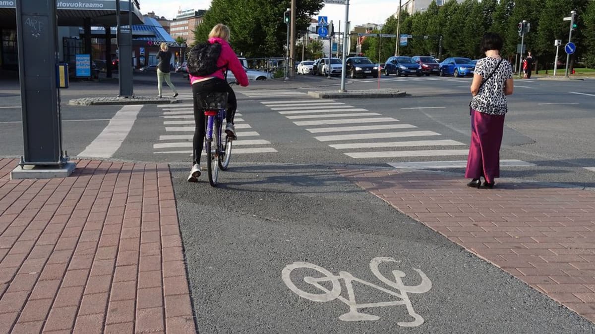 Pyöräilijä ja jalankulkija odottavat vihreää valoa suojatien laidassa 