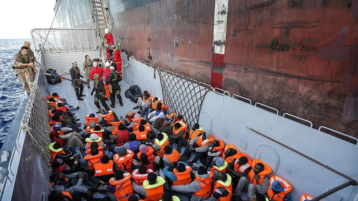 kymmeniä ihmisiä istuu laivan kannella pelastuliiviin pukeutuneena