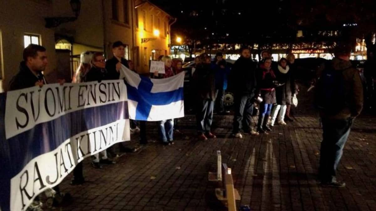 Mielenosoittajat kaupungintalon ulkopuolella. Bannerissa lukee Suomi ensin - rajat kiinni.