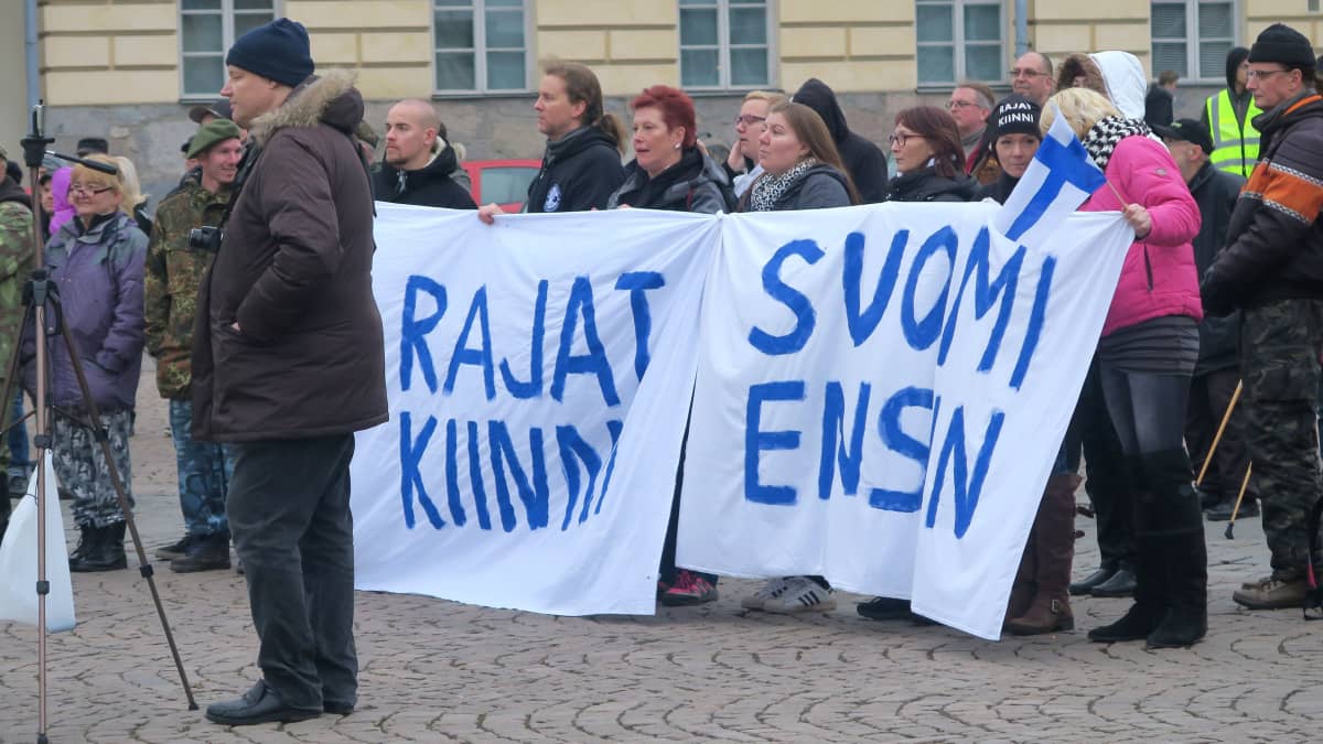 Mielenosoittajat pitävät lakanoita, joissa tekstit rajat kiinni ja Suomi ensin
