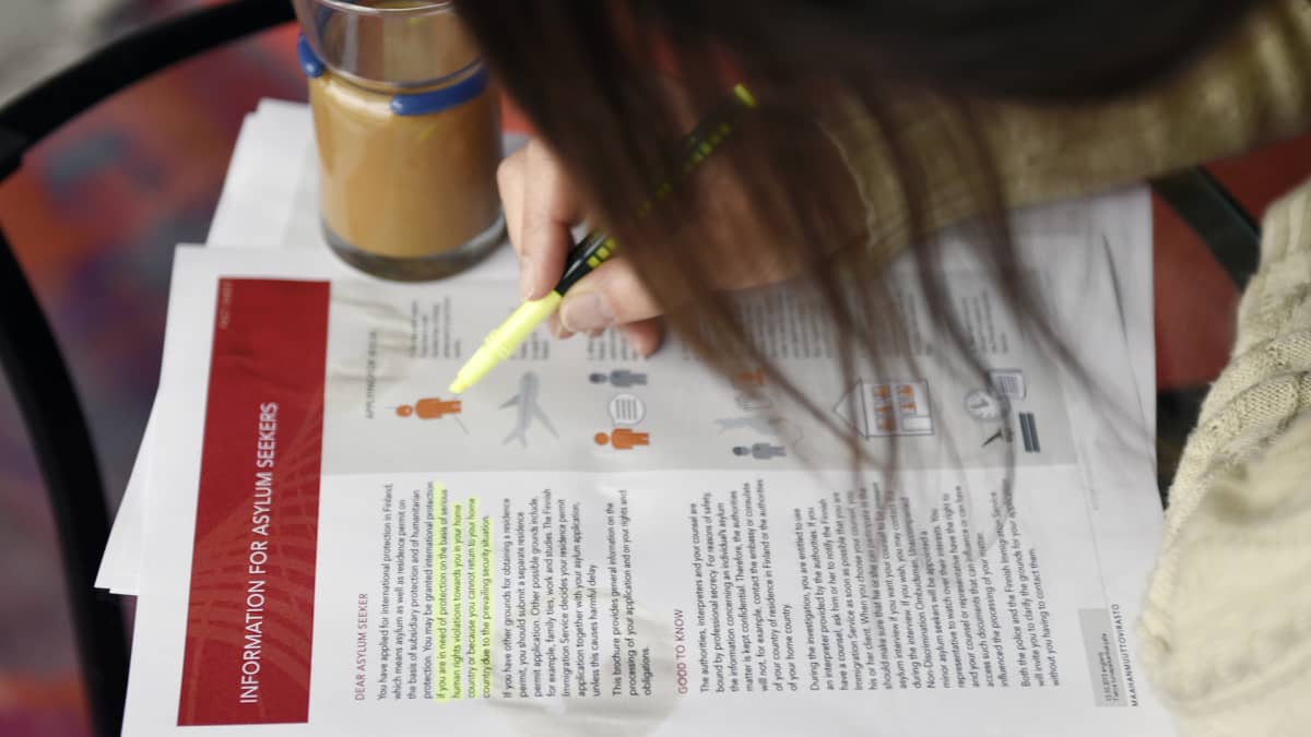 Nainen tutkii maahanmuuttoviraston infopakettia liittyen turvapaikan hakemiseen Suomesta.