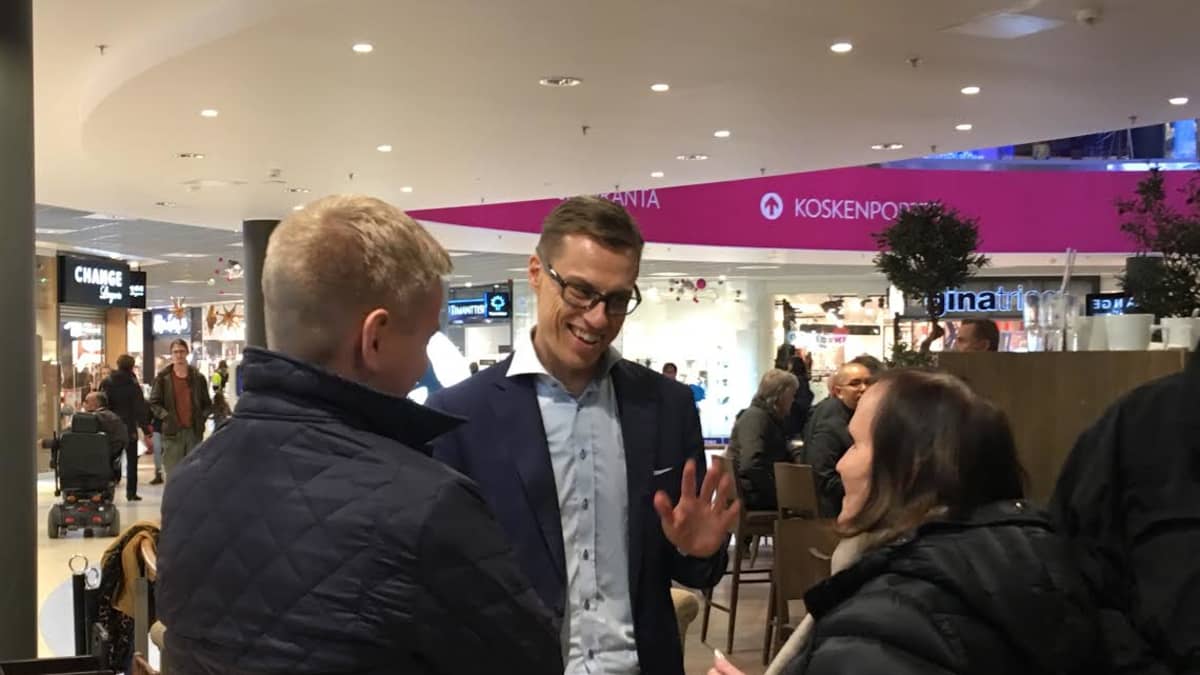 Alexander Stubb puhuu ihmisten kanssa märässä paidassa