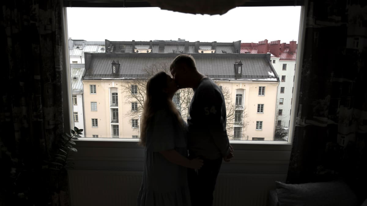 Pariskunta suutelee ikkunan edessä.