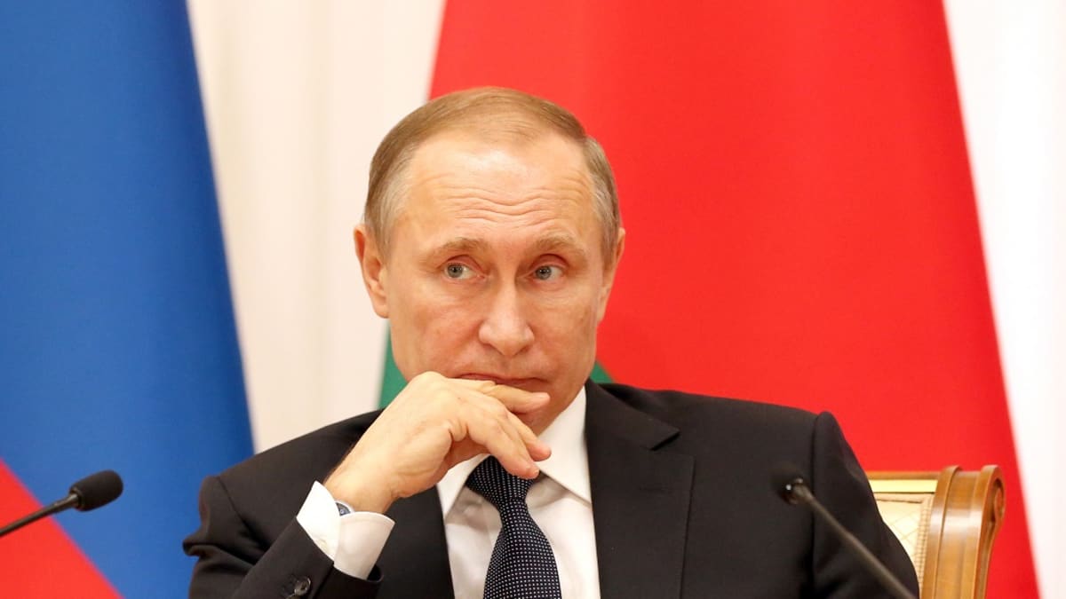 Putin istuu tummassa puvussa mietteliään näköisenä, oikea käsi leuallaan. Taustalla näkyvät Venäjän ja Valko-Venäjän liput. Hänen edessään on kaksi mikrofonia.