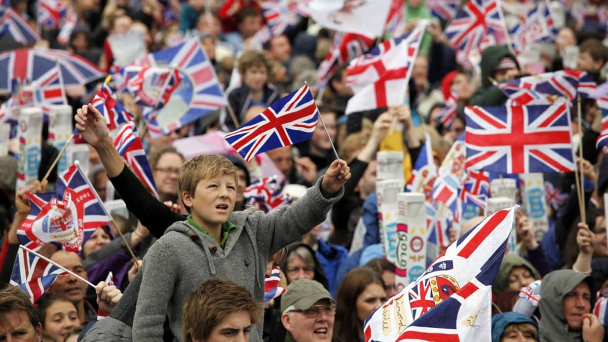 Suuri ihmisjoukko heiluttaa Britannian ja Eglannin lippuja. 
