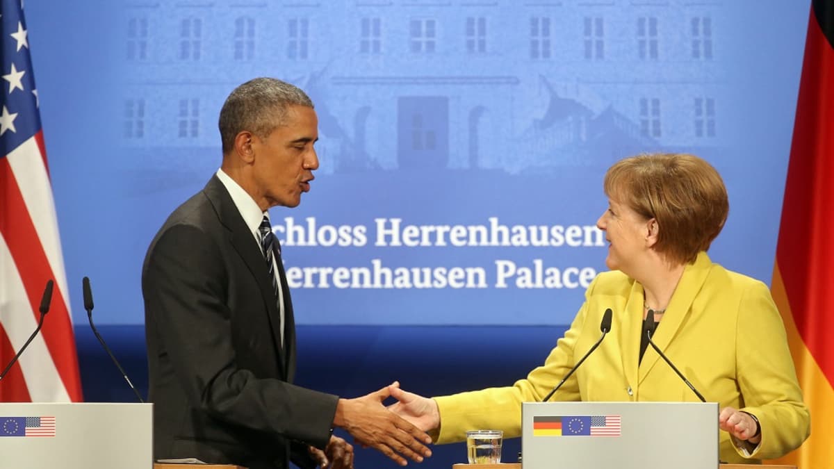 Puhujakorokkeella seisovat Obama ja Merkel kättelevät. Taustalle on heijastettu Herrenhausenin linnan julkisivun kuva. 