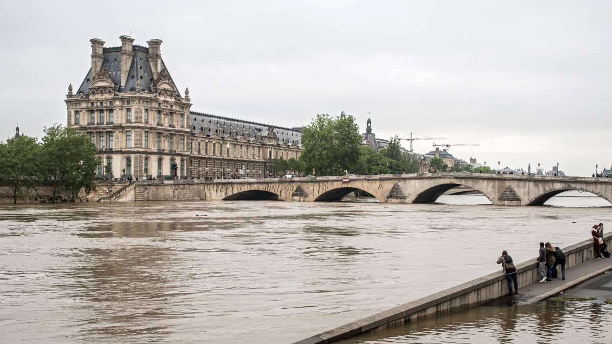 Seinejoki, jossa pinta noussut, joen takana Louvren taidemuseo. Etualalla joitakin ihmisiä katselemassa ja ottamassa kuvaa.