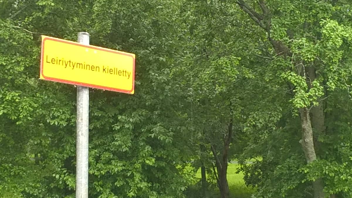 Leiriytyminen kielletty -kyltti puistoalueen reunassa.