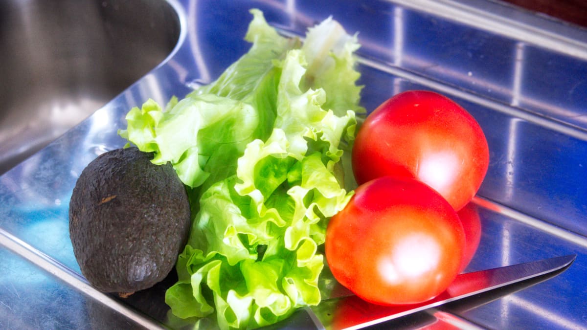 Avokado, salaaattia ja tomaatteja tiskipöydällä.