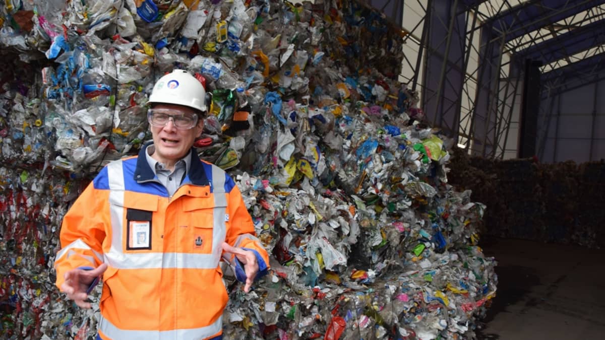 Mies kertoo Ekokemin Muovijalostamosta muovijätepaaleja taustallaan