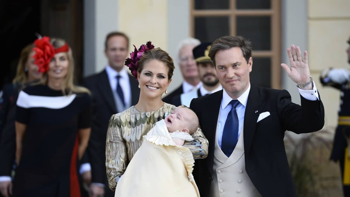Madeleine lapsi sylissään, Chris vilkuutta vieressä.