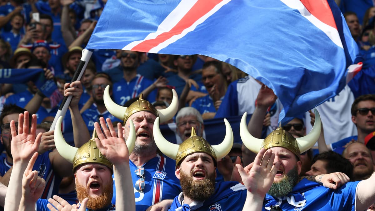 Islantilannin lipun väreihin pukeutuneita jalkapallofaneja. Etuan miesjoukolla on viikinkihatut ja he heiluttavat Islannin lippua.