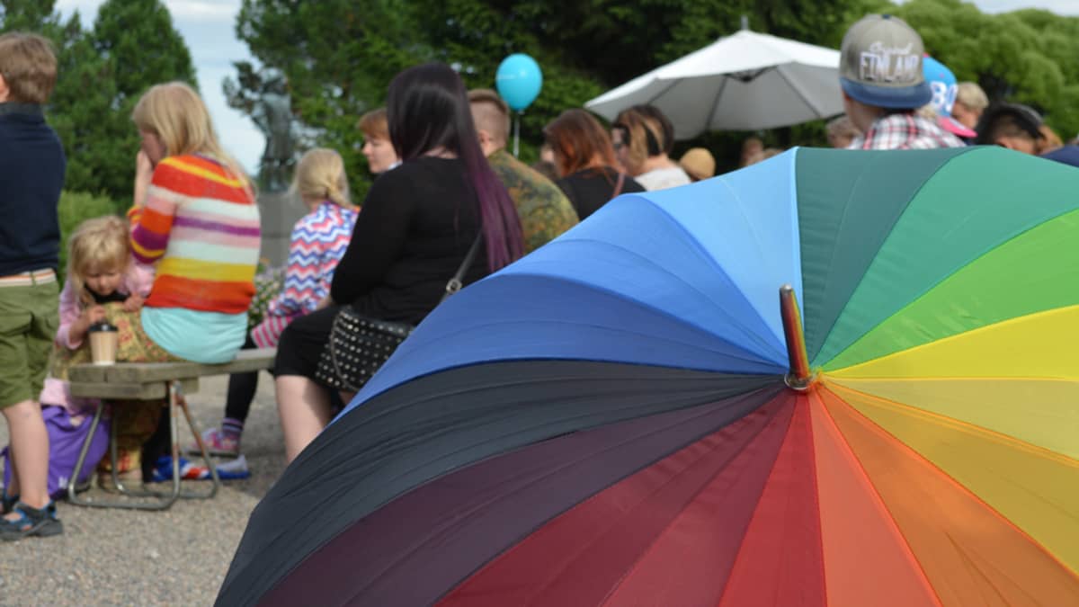 Sateenkaaren värinen sateenvarjo ja ihmisiä.