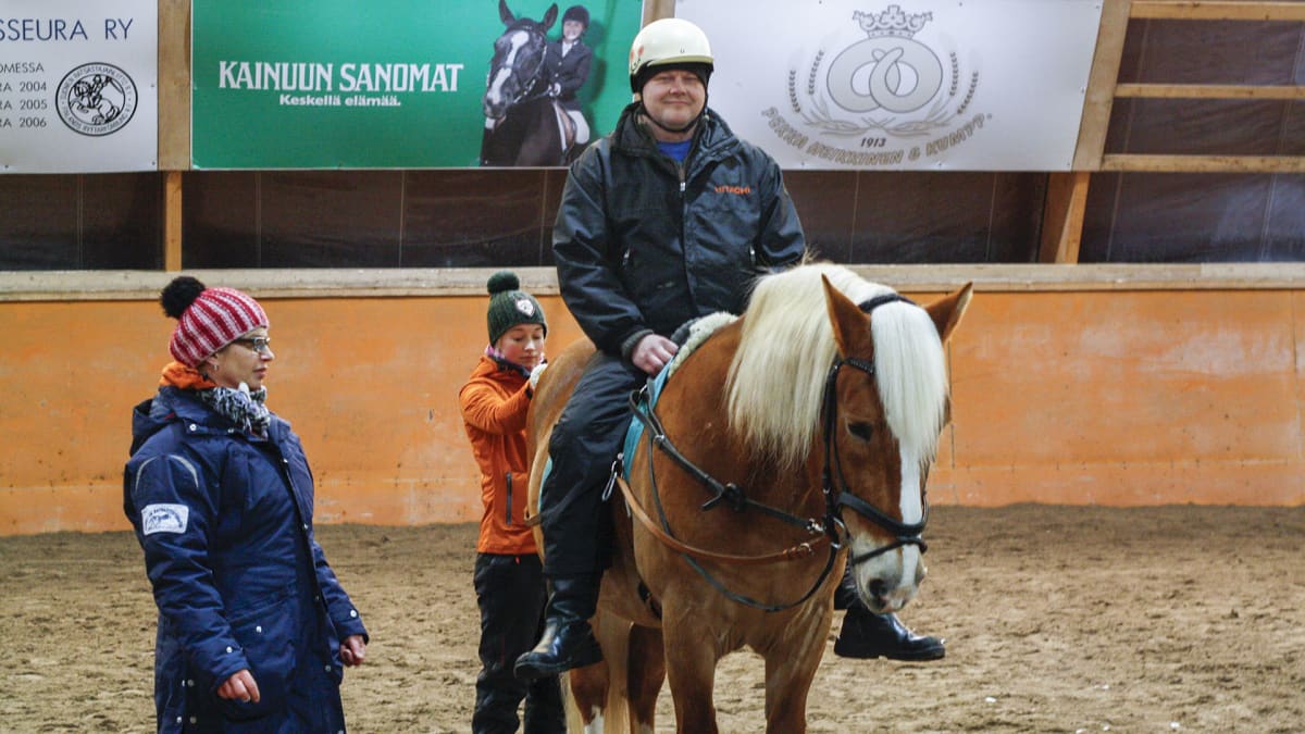 Ratsastusterapia-tutkimukseen osallistuva mies hevosen selässä. Kaksi naista seisoo hevosen vieressä.